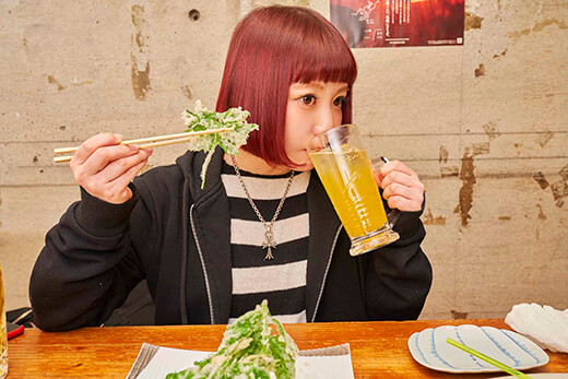 あしたば天ぷらを持ちながら、パッションジュースを飲む小鳥遊さん